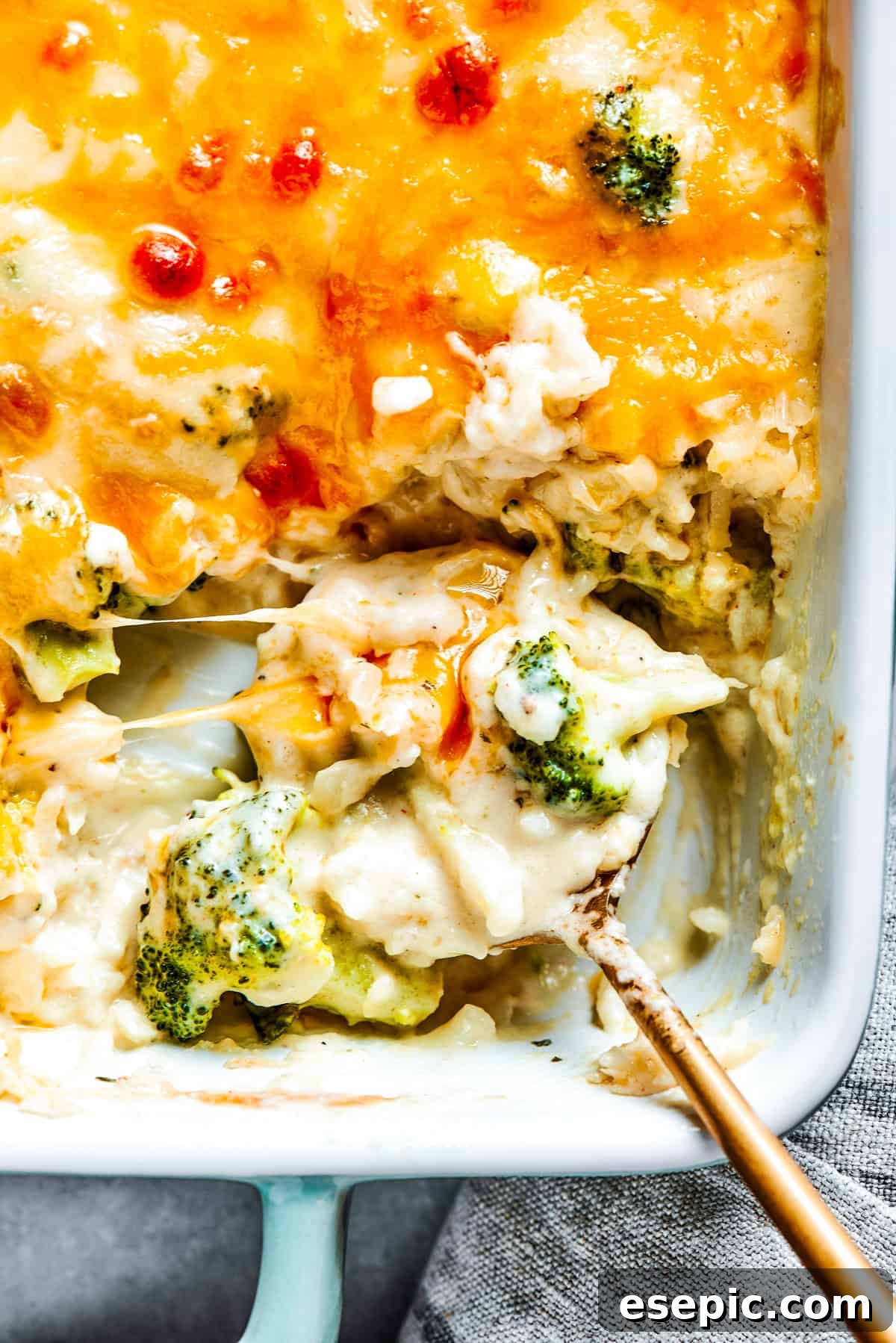A serving spoon scoops out a generous portion of freshly baked broccoli rice casserole from a hot baking dish, steam gently rising.