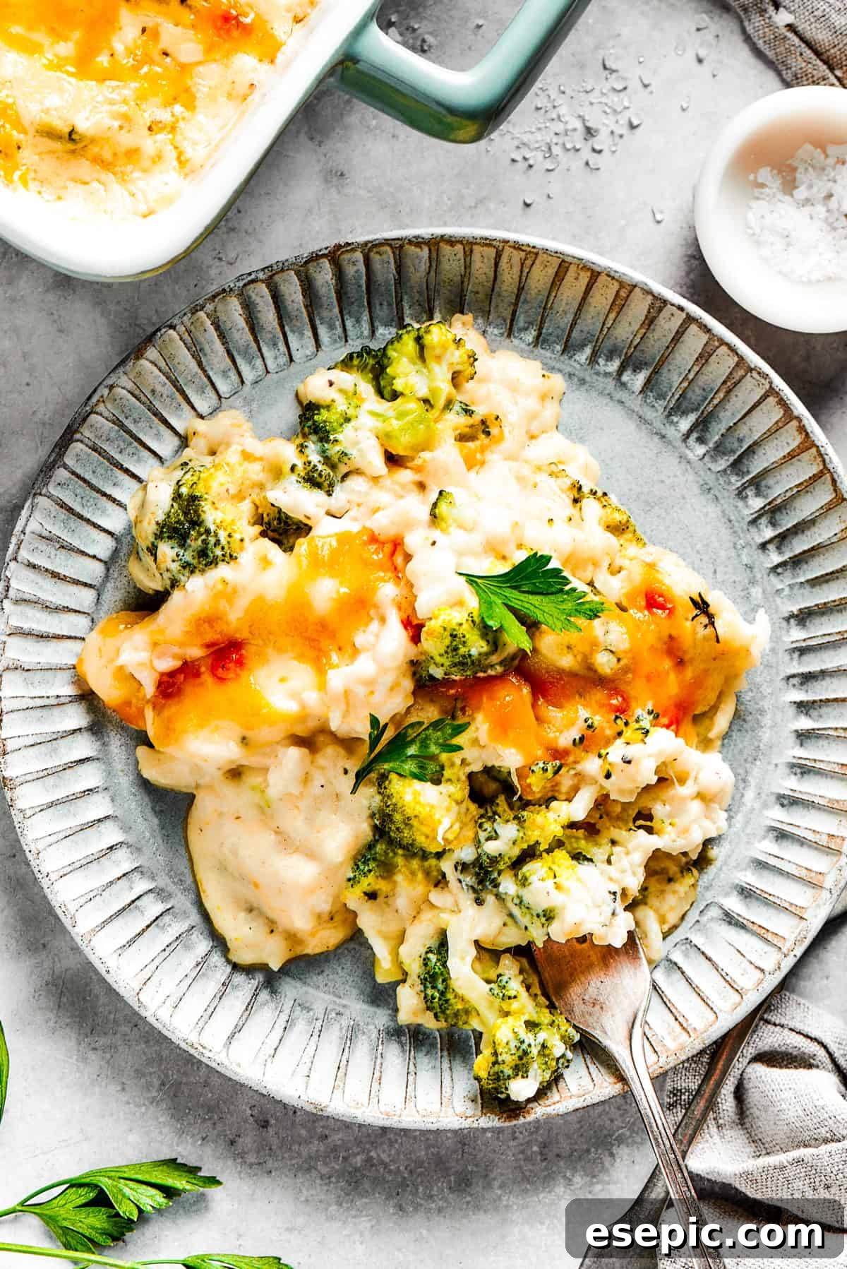 A generous serving of creamy broccoli & rice casserole on a vibrant blue plate, with a fork ready to dig in.