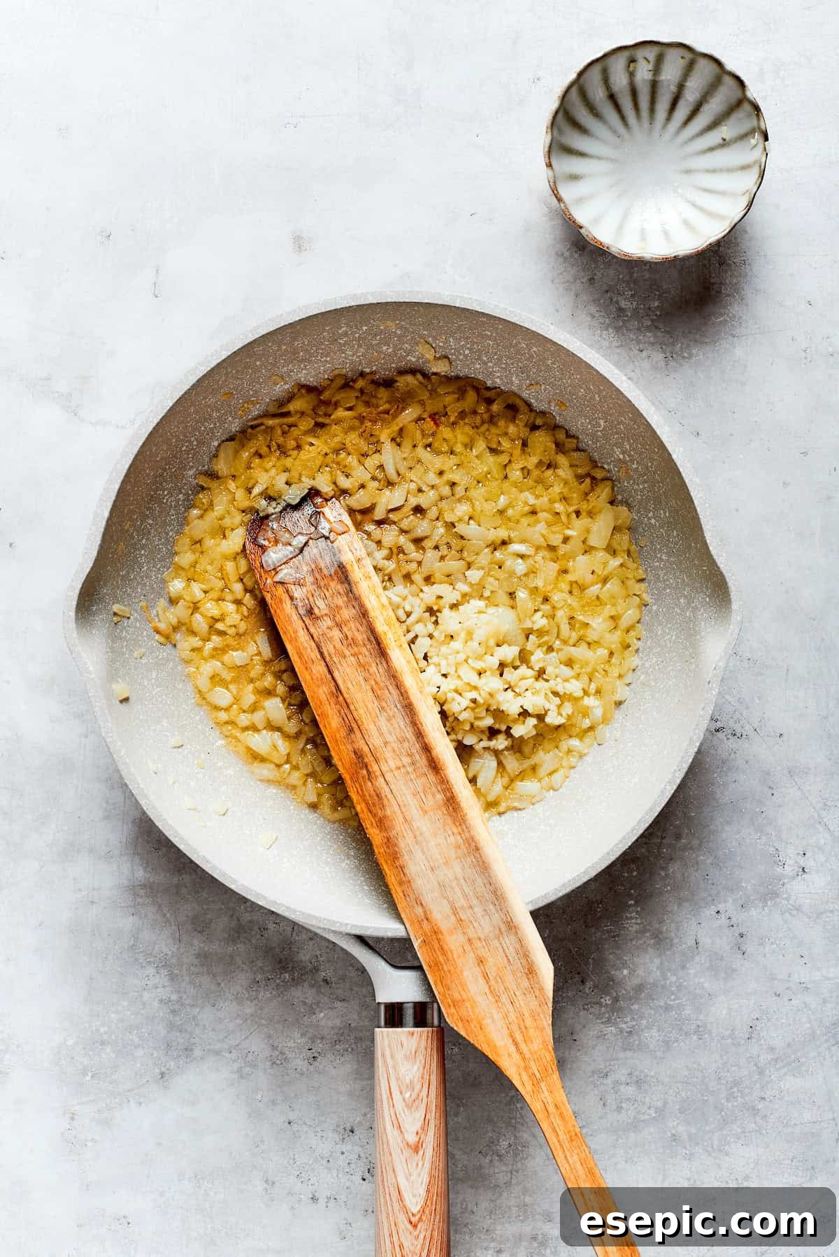 Garlic and diced onion are gently stirred in a skillet with melted butter, creating a fragrant base for the casserole sauce.
