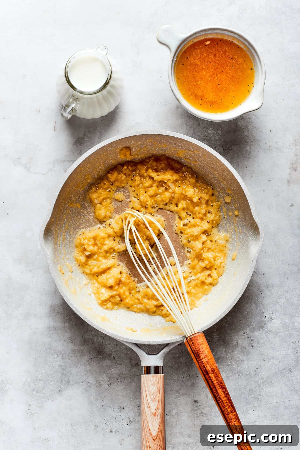 Flour is whisked into the sautéed onion and garlic mixture in a skillet, forming a golden roux to thicken the sauce.