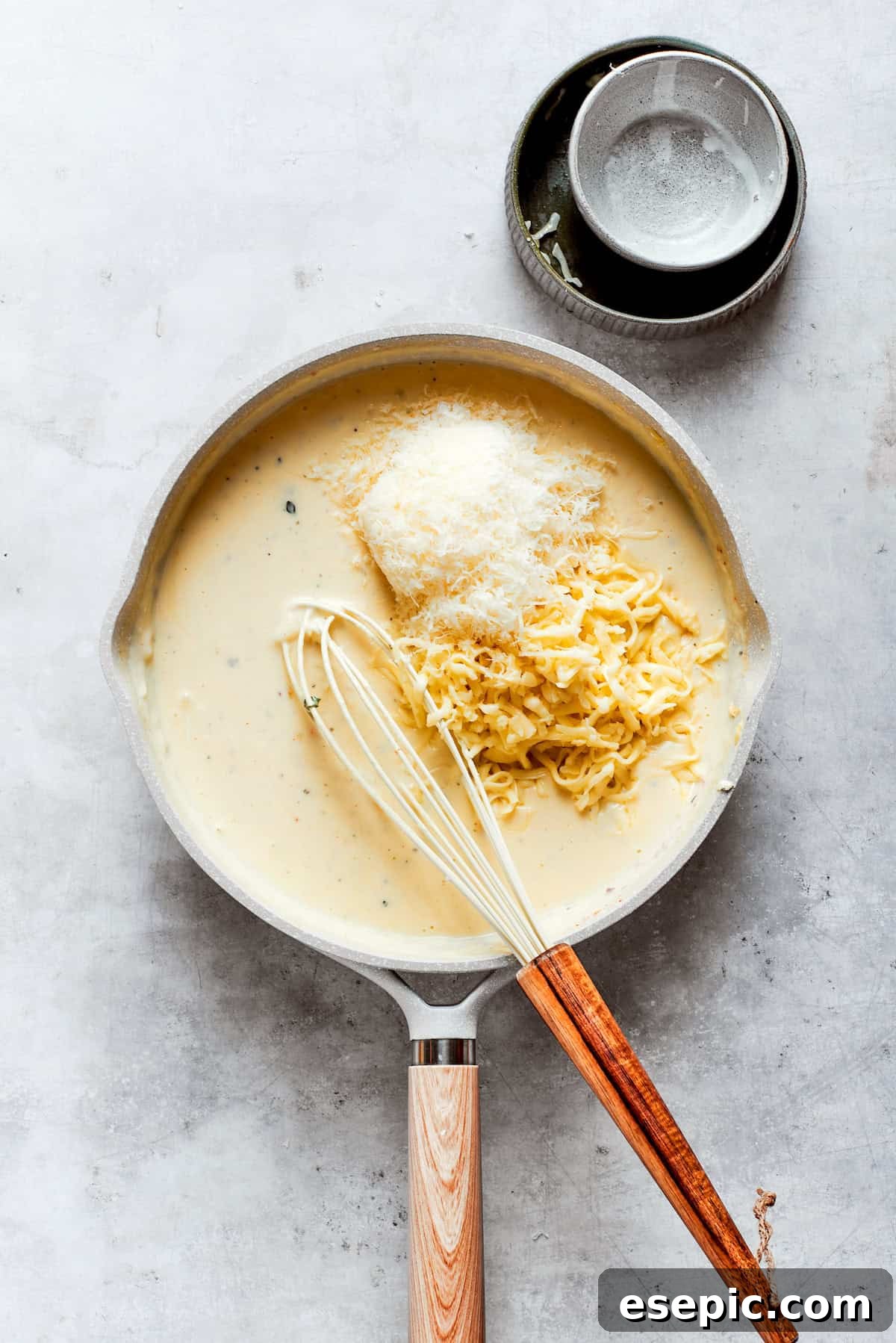 Various shredded cheeses are gently folded into the thickened sauce in a pot, creating a rich and gooey consistency.
