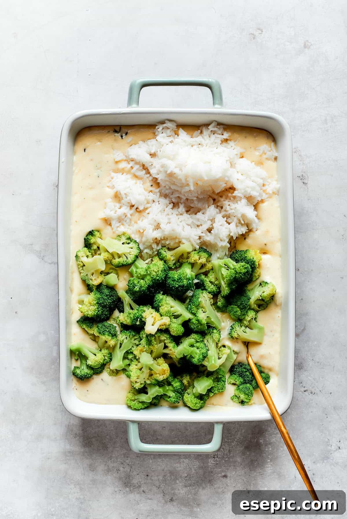 A baking pan filled with creamy cheese sauce, ready for the addition of cooked broccoli and rice.