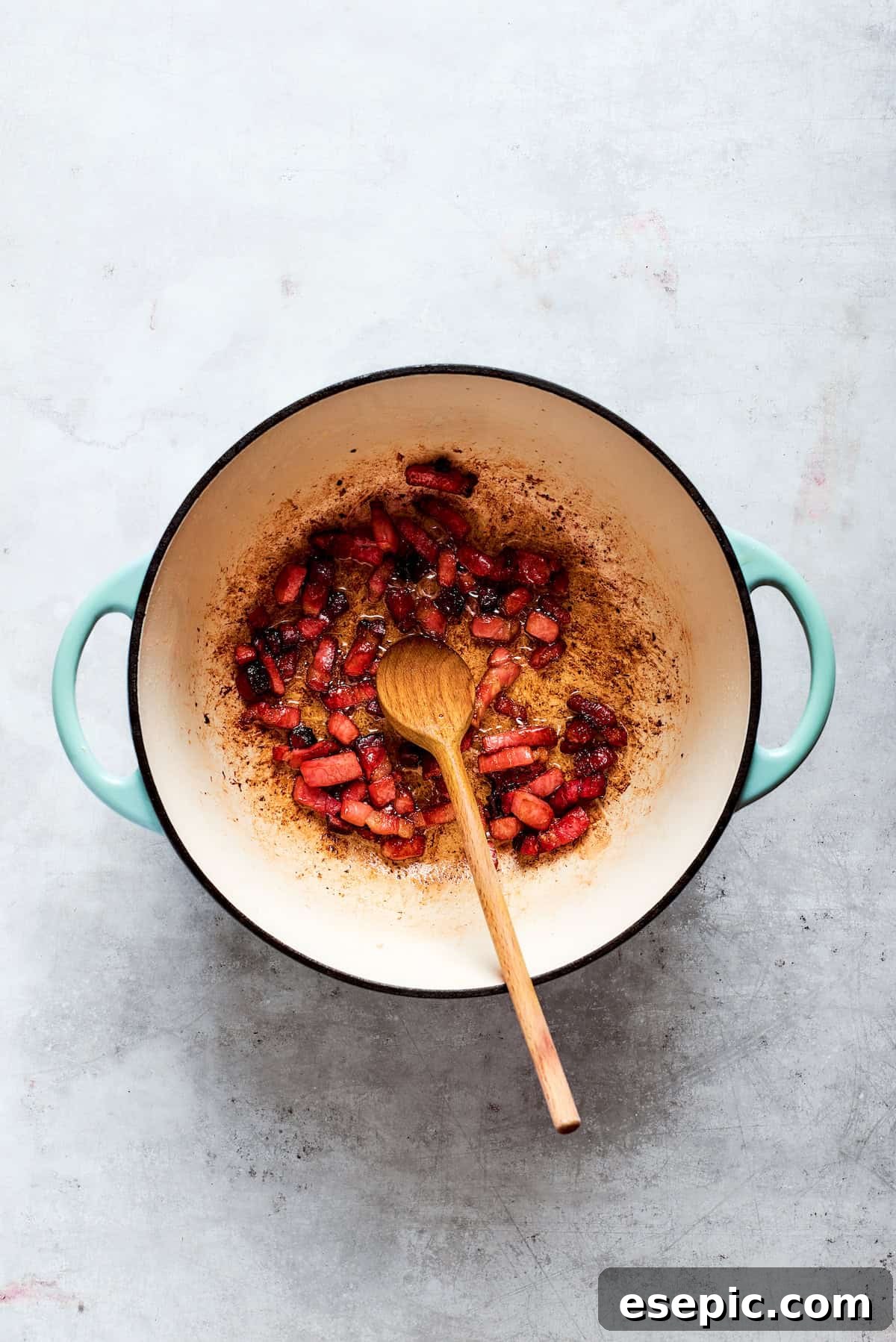 A spoon stirs chopped bacon in a pot, beginning the cooking process for Zuppa Toscana.