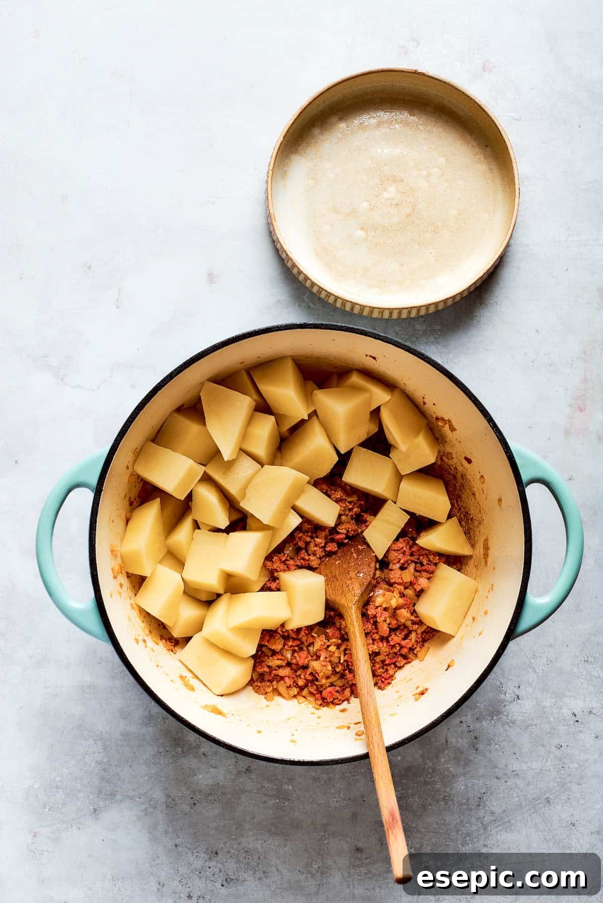 Diced potatoes are added to the browned Italian sausage in the pot, building the base of the soup.