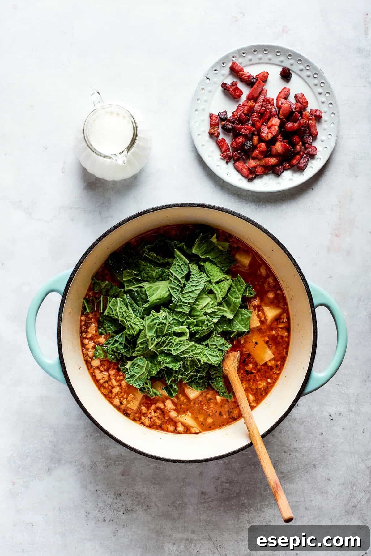 Fresh kale is added to the top of the simmering soup pot, preparing to wilt into the broth.