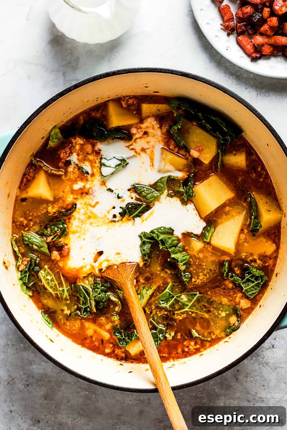 Heavy cream is stirred into a pot of creamy soup with diced potatoes, completing the rich base of Zuppa Toscana.