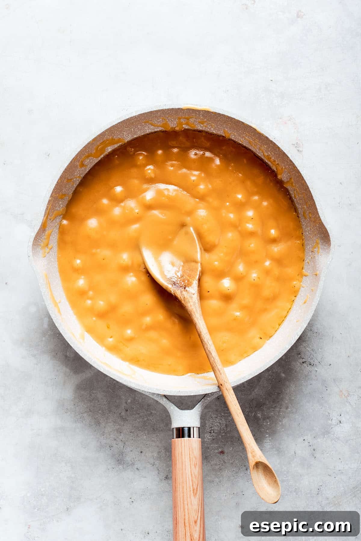 Millionaire Bars are decadent layers of homemade buttery shortbread, creamy caramel, and thick chocolate ganache. Smooth, golden caramel sauce being stirred in a pot, showing its thick, glossy texture.