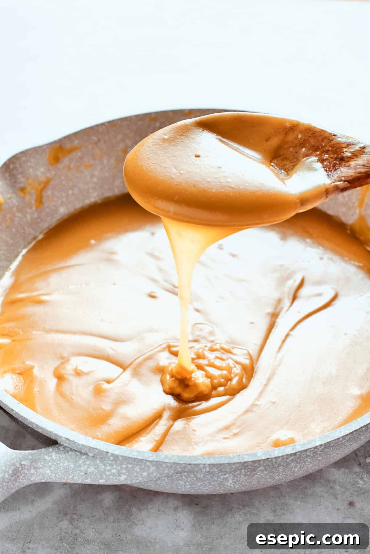 Millionaire Bars are decadent layers of homemade buttery shortbread, creamy caramel, and thick chocolate ganache. A spoon lifting a stream of thick, golden caramel sauce, demonstrating its rich consistency.