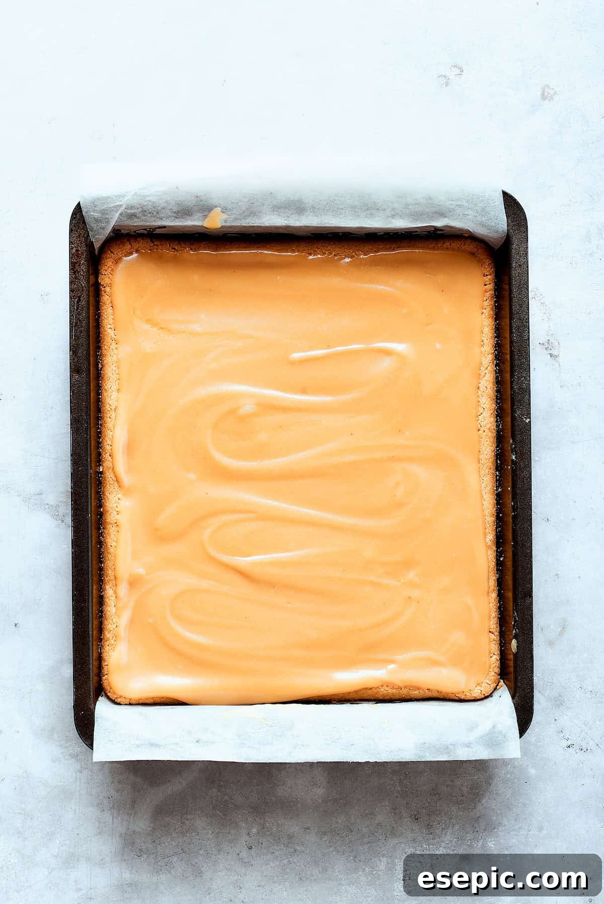 Millionaire Bars are decadent layers of homemade buttery shortbread, creamy caramel, and thick chocolate ganache. Pouring homemade caramel sauce evenly over a cooled shortbread crust in a baking pan.