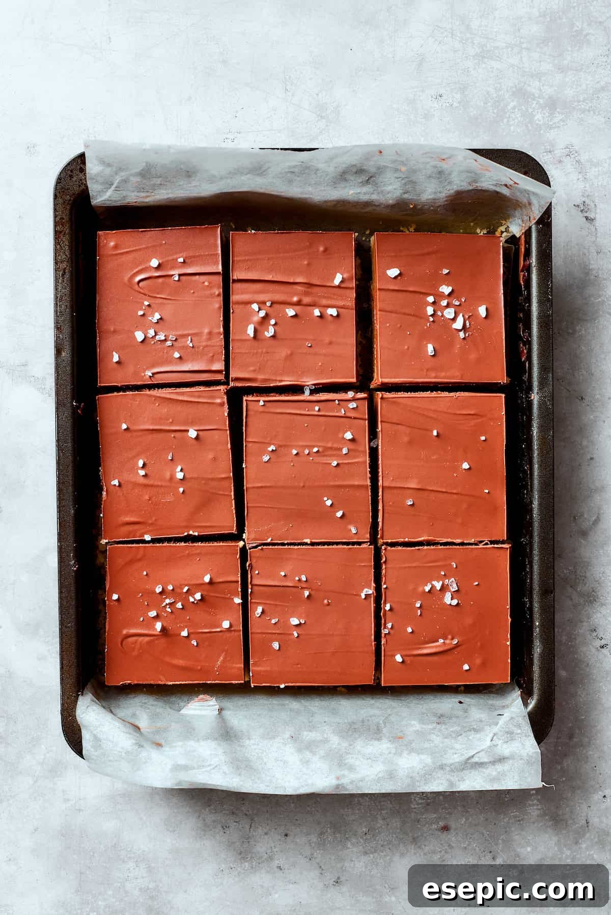 Millionaire Bars are decadent layers of homemade buttery shortbread, creamy caramel, and thick chocolate ganache. A pan of Millionaire Bars topped with a smooth layer of chocolate ganache and a sprinkle of flaky sea salt.