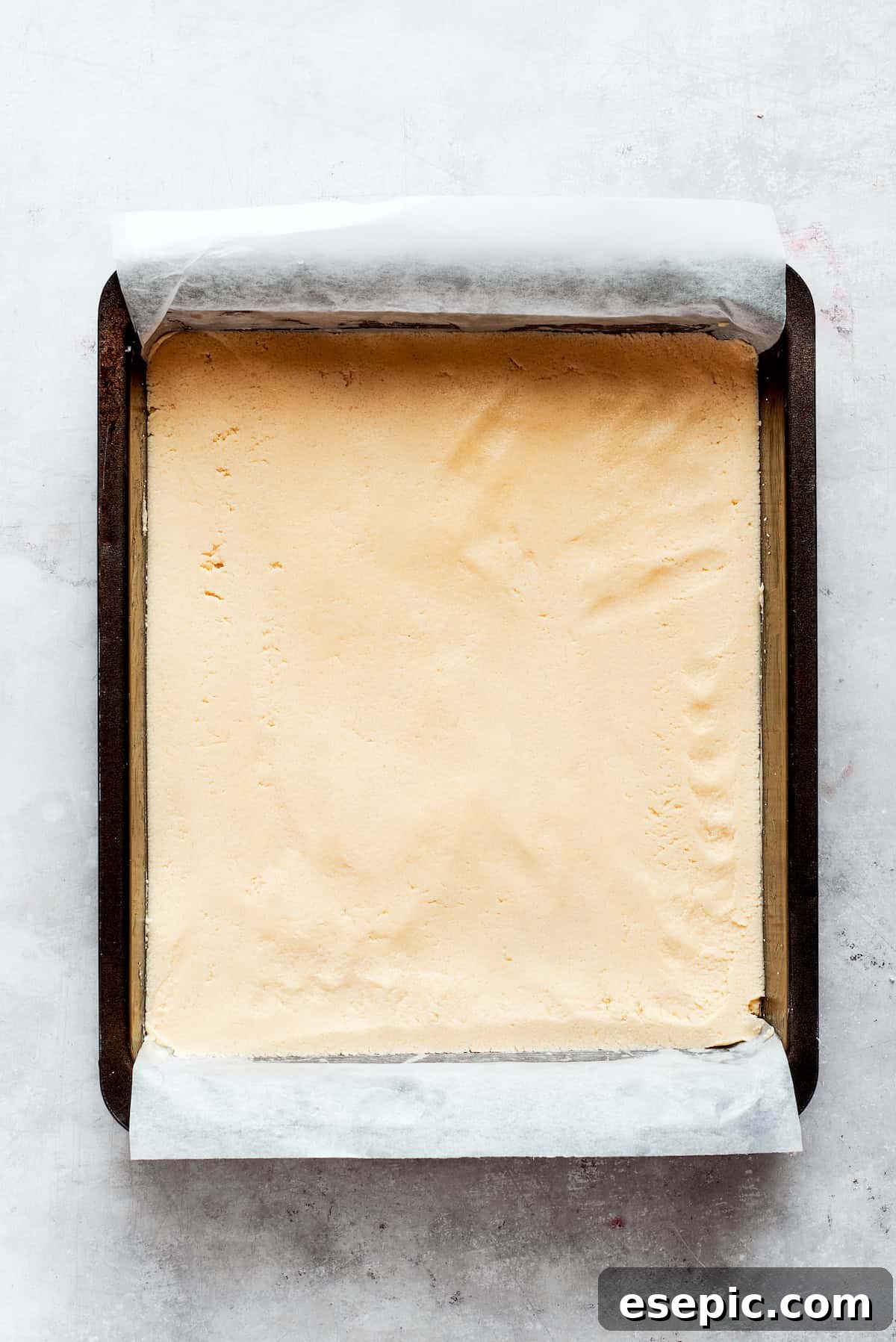 Millionaire Bars are decadent layers of homemade buttery shortbread, creamy caramel, and thick chocolate ganache. Shortbread dough being pressed evenly into a parchment-lined baking pan.