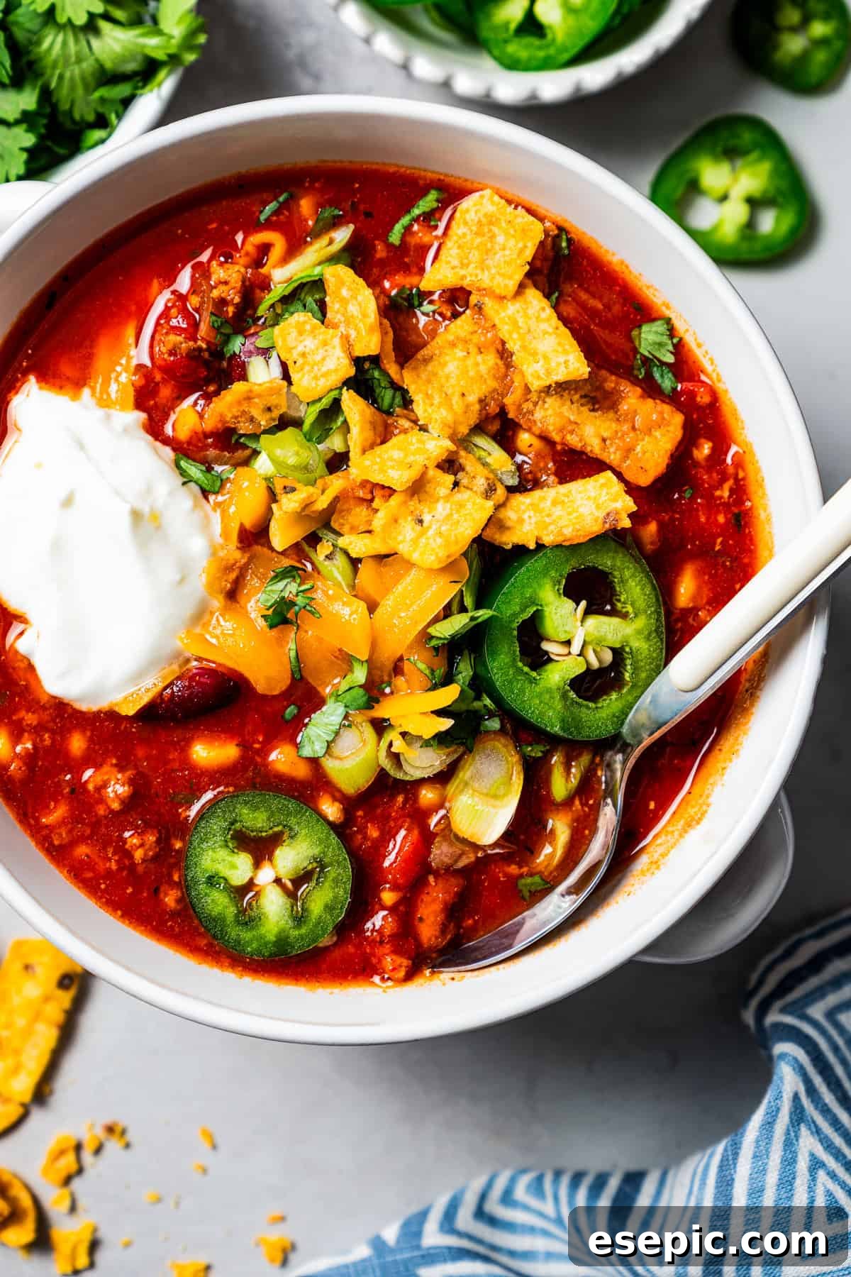 Overhead image of a bowl of turkey chili garnished with sour cream, jalapeños, and corn chips.