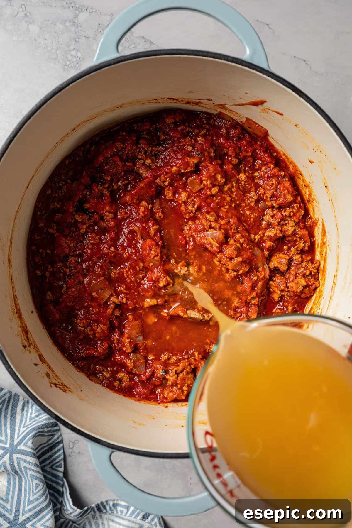Chicken broth being poured over the other turkey chili ingredients in a pot.