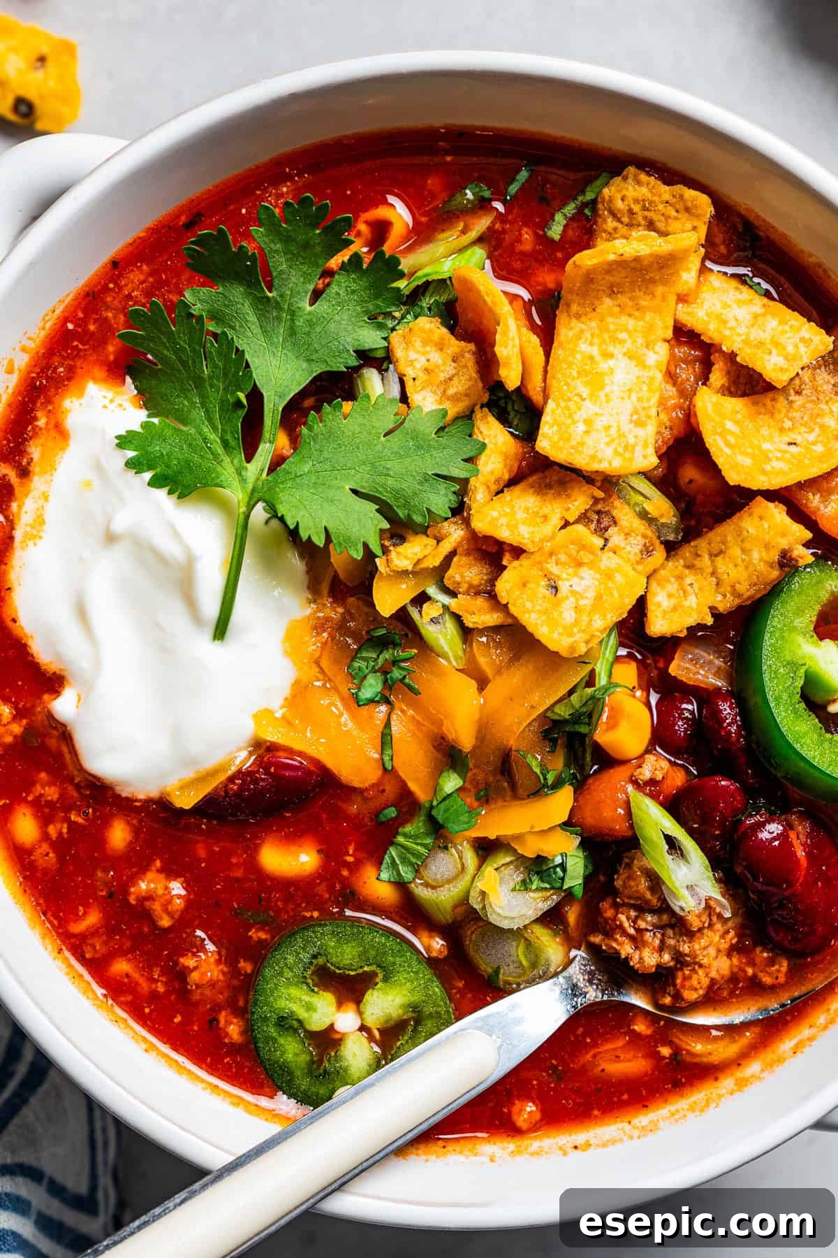 Overhead close up view of a bowl of turkey chili garnished with sour cream, jalapeños, and corn chips.