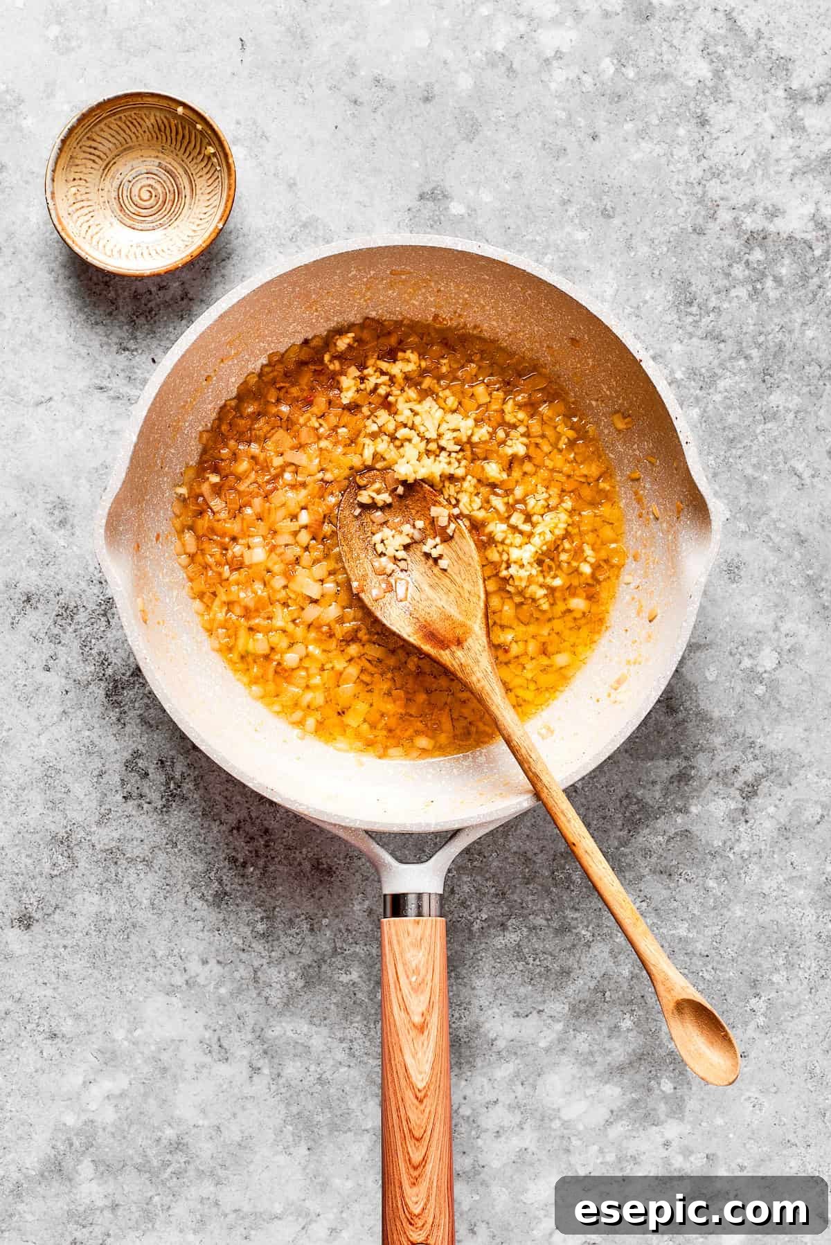 Smothered Chicken breasts feature pan-fried chicken in a crispy breadcrumb coating topped with a rich and creamy homemade gravy. Chopped garlic and shallot are added to a hot pan with melted butter, beginning to sauté.