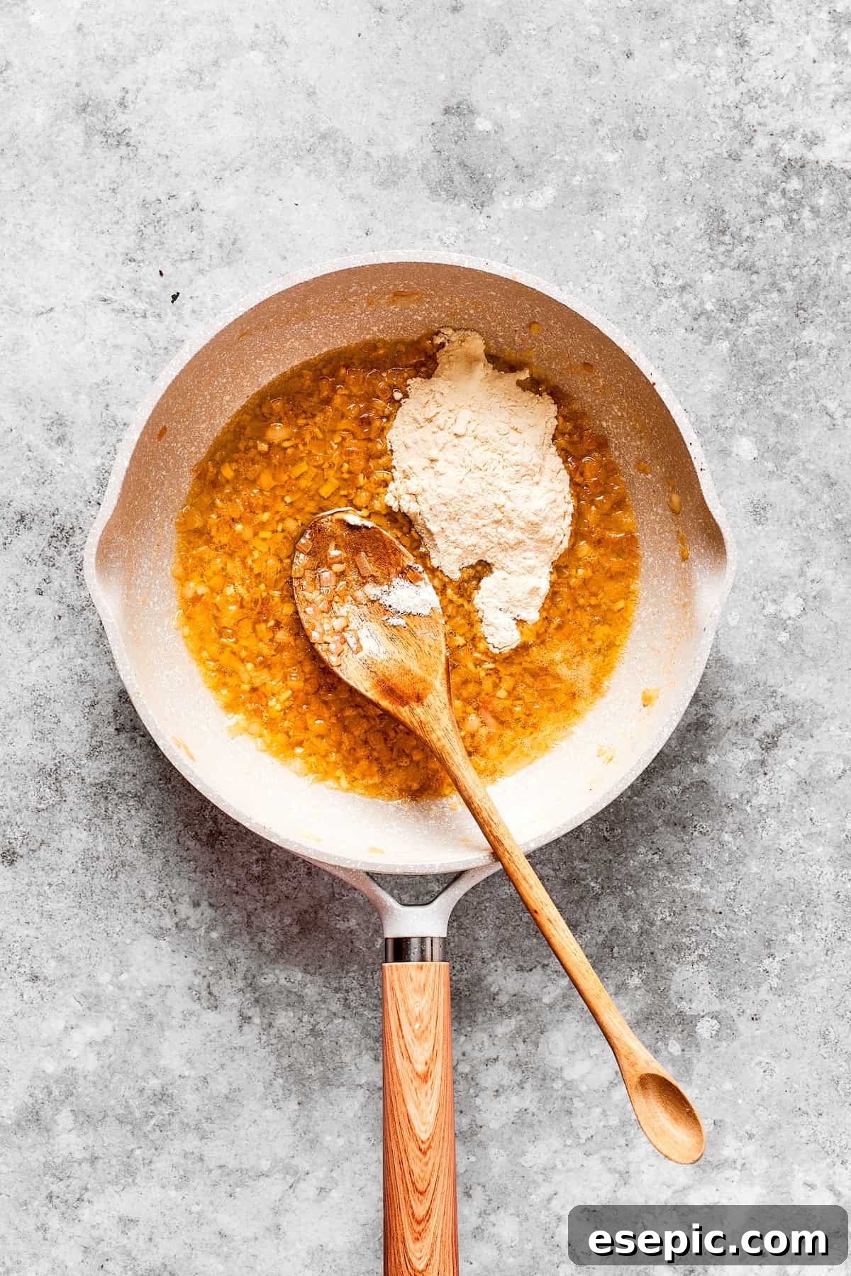 Smothered Chicken breasts feature pan-fried chicken in a crispy breadcrumb coating topped with a rich and creamy homemade gravy. Flour is carefully sprinkled into a pan with sautéed aromatics and melted butter, forming the base of a roux.