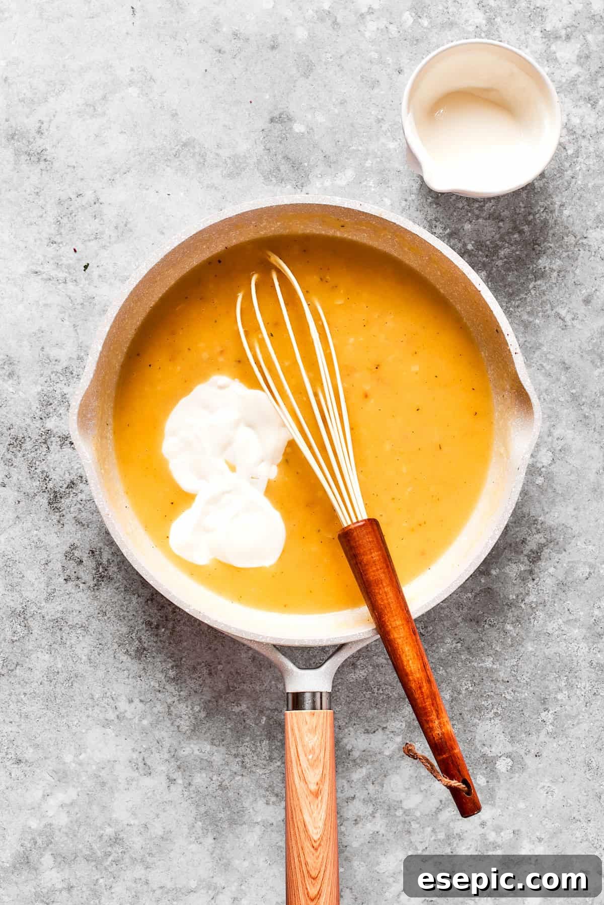 Smothered Chicken breasts feature pan-fried chicken in a crispy breadcrumb coating topped with a rich and creamy homemade gravy. Half and half is being whisked into a thickening gravy mixture in a pan, creating a creamy texture.