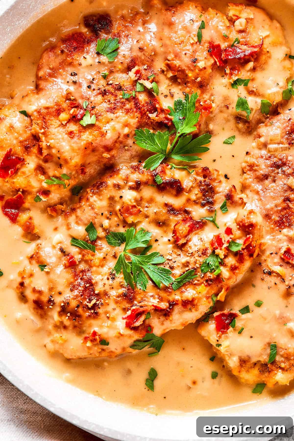 Smothered Chicken breasts feature pan-fried chicken in a crispy breadcrumb coating topped with a rich and creamy homemade gravy. Fresh parsley leaves are sprinkled over pieces of rich, creamy smothered chicken, adding a vibrant garnish.