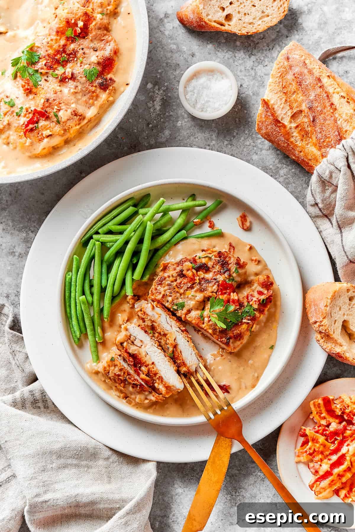 Smothered Chicken breasts feature pan-fried chicken in a crispy breadcrumb coating topped with a rich and creamy homemade gravy. A plate of smothered chicken with crisp green beans, beautifully arranged on a rustic wooden table.