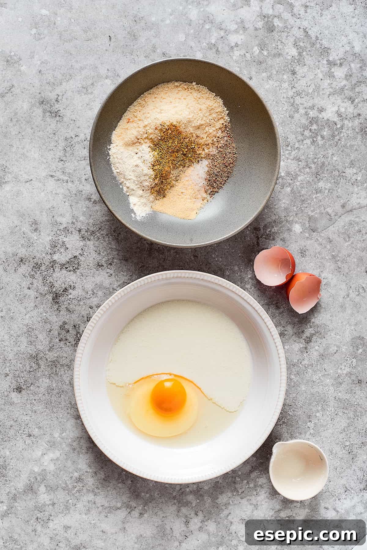 Smothered Chicken breasts feature pan-fried chicken in a crispy breadcrumb coating topped with a rich and creamy homemade gravy. A bowl containing a mixture of breadcrumbs and seasonings sits next to a bowl of whisked egg and buttermilk, ready for dredging.