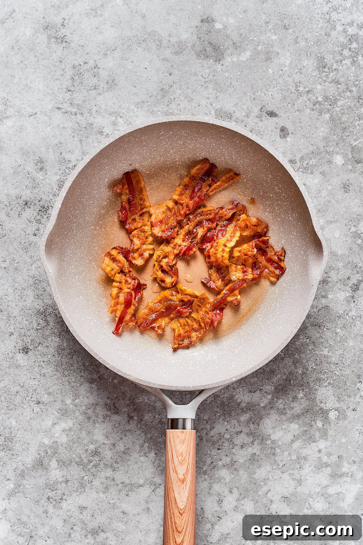 Smothered Chicken breasts feature pan-fried chicken in a crispy breadcrumb coating topped with a rich and creamy homemade gravy. Diced bacon is sizzling and cooking in a hot skillet, rendering its fat and becoming crispy.