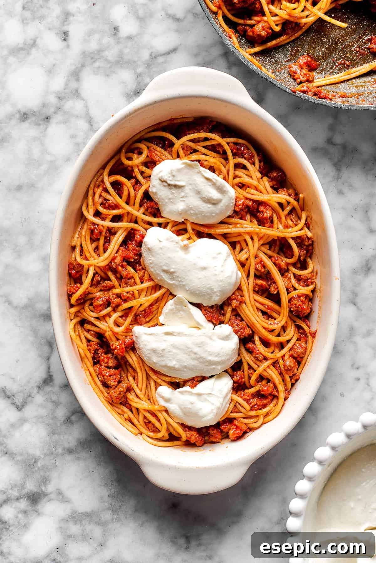 Cooked spaghetti tossed with meat sauce, topped with a layer of creamy cheese mixture in a baking dish.
