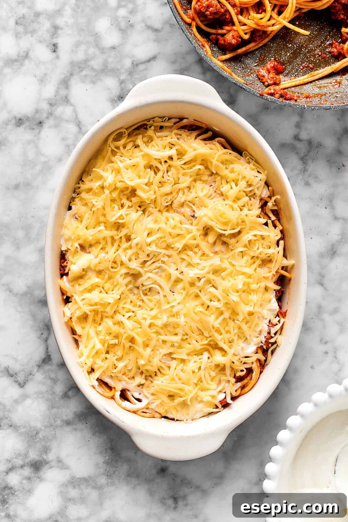 A layer of shredded mozzarella cheese covering the spaghetti and cheese mixture in a 9x13 inch baking dish.