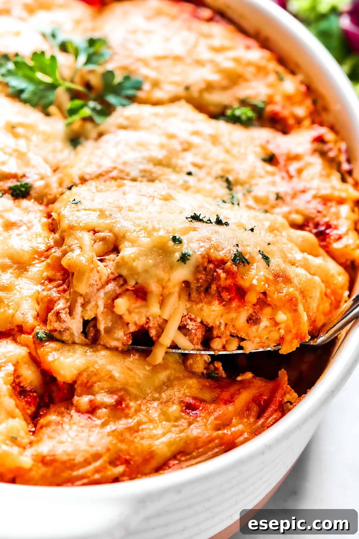 A large serving spoon scooping out a portion of baked million dollar spaghetti from a casserole dish, showing the cheesy layers.