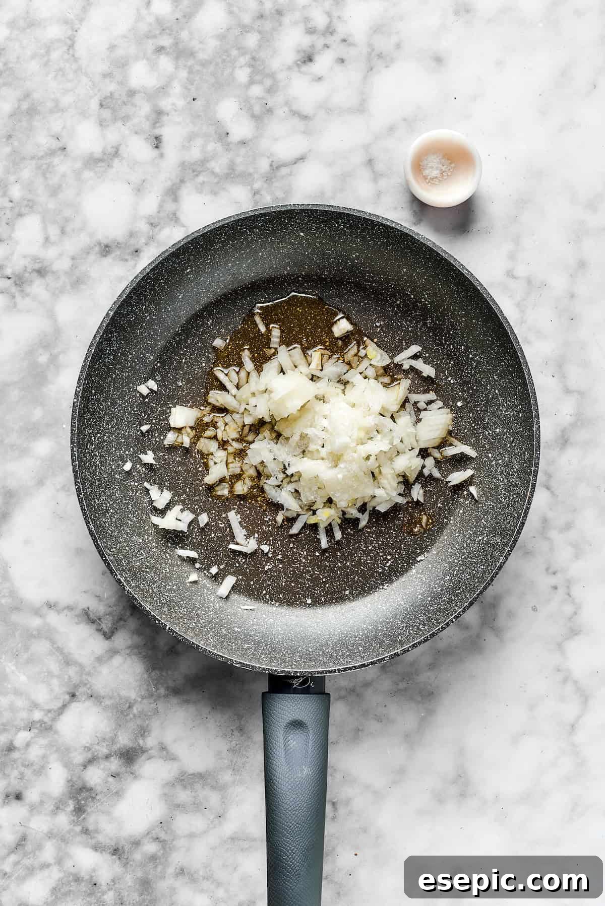 Diced onions in a skillet, ready to be sautéed until translucent.