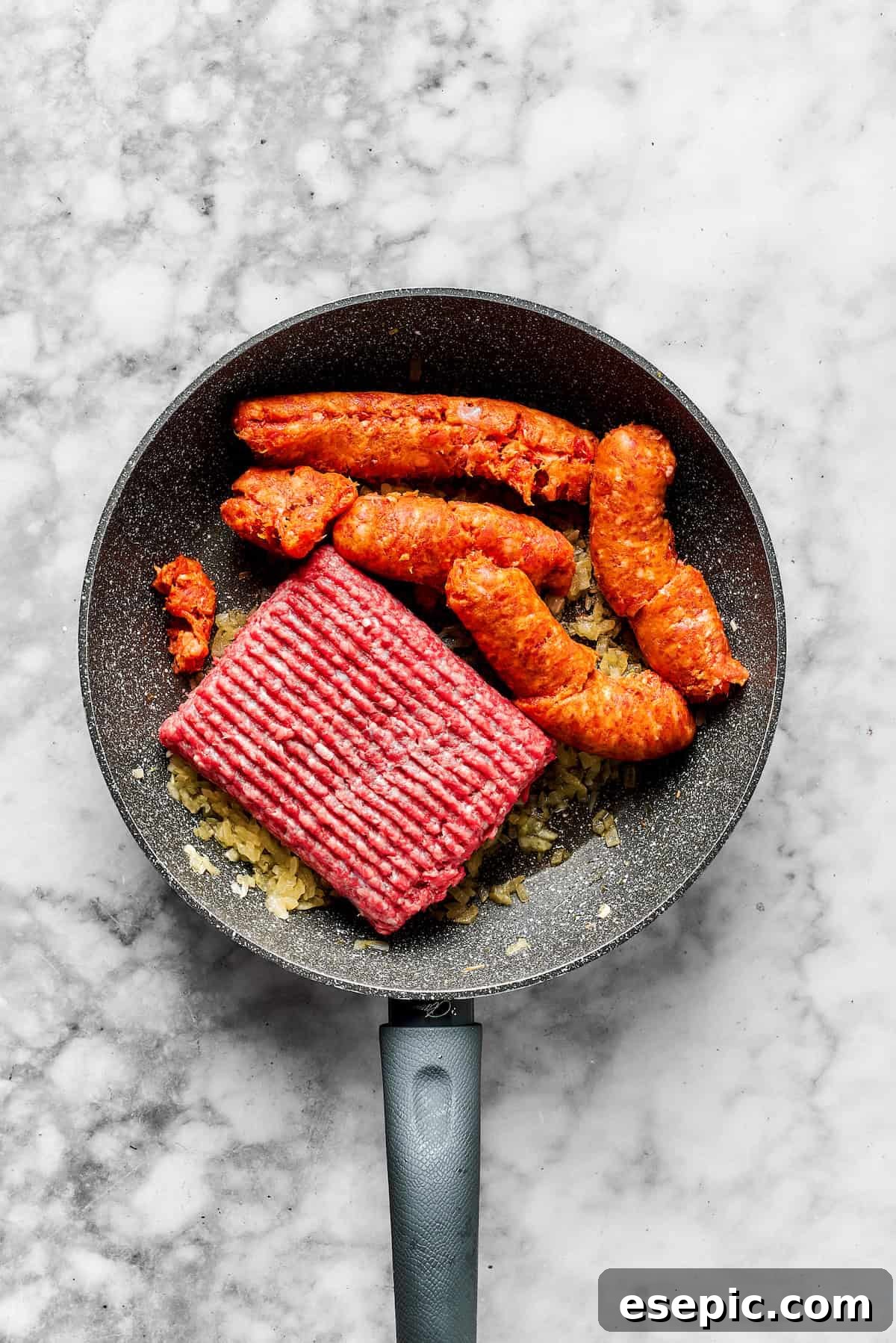 Adding ground beef and Italian sausage to a skillet with sautéed onions.