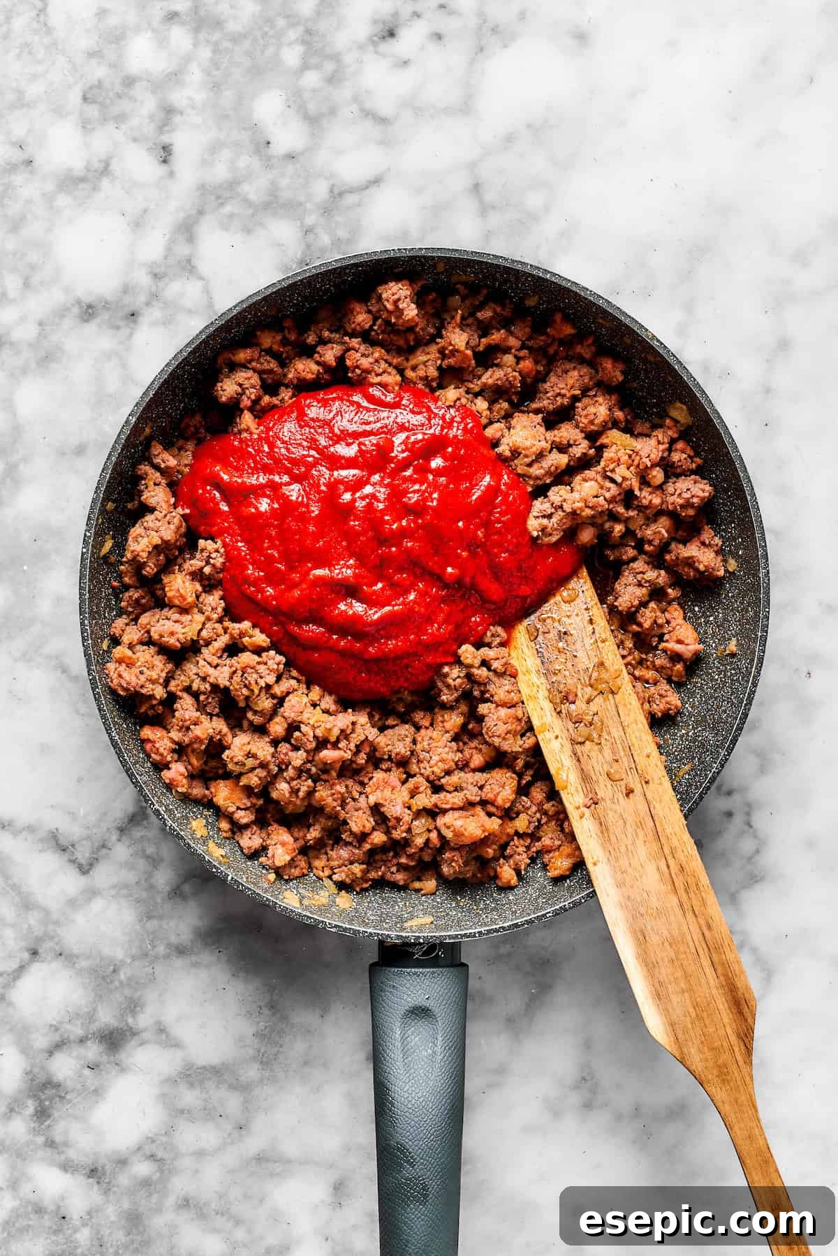 Marinara sauce being poured into a skillet with cooked meat and onions.