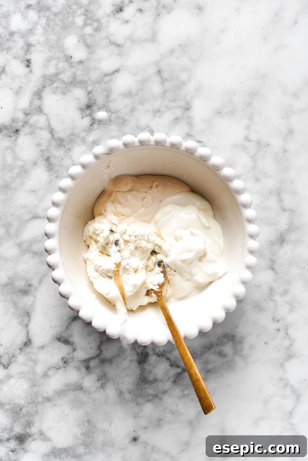 Ricotta cheese, cream cheese, and sour cream being mixed in a white bowl for the cheesy layer.