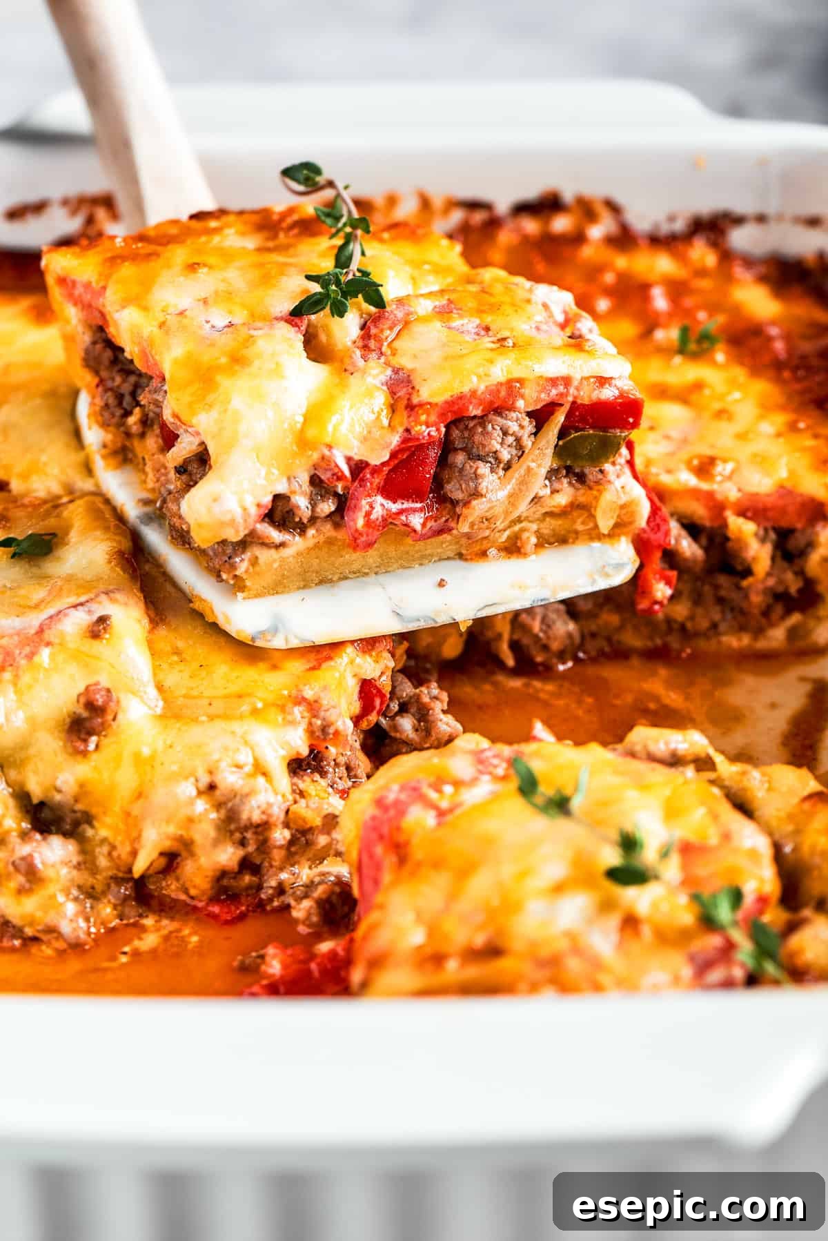 A perfectly portioned slice of John Wayne Casserole, showcasing its distinct layers of flaky biscuit, savory ground beef, vegetables, sour cream, and melted cheese, being carefully lifted from the baking dish, ready to be served.