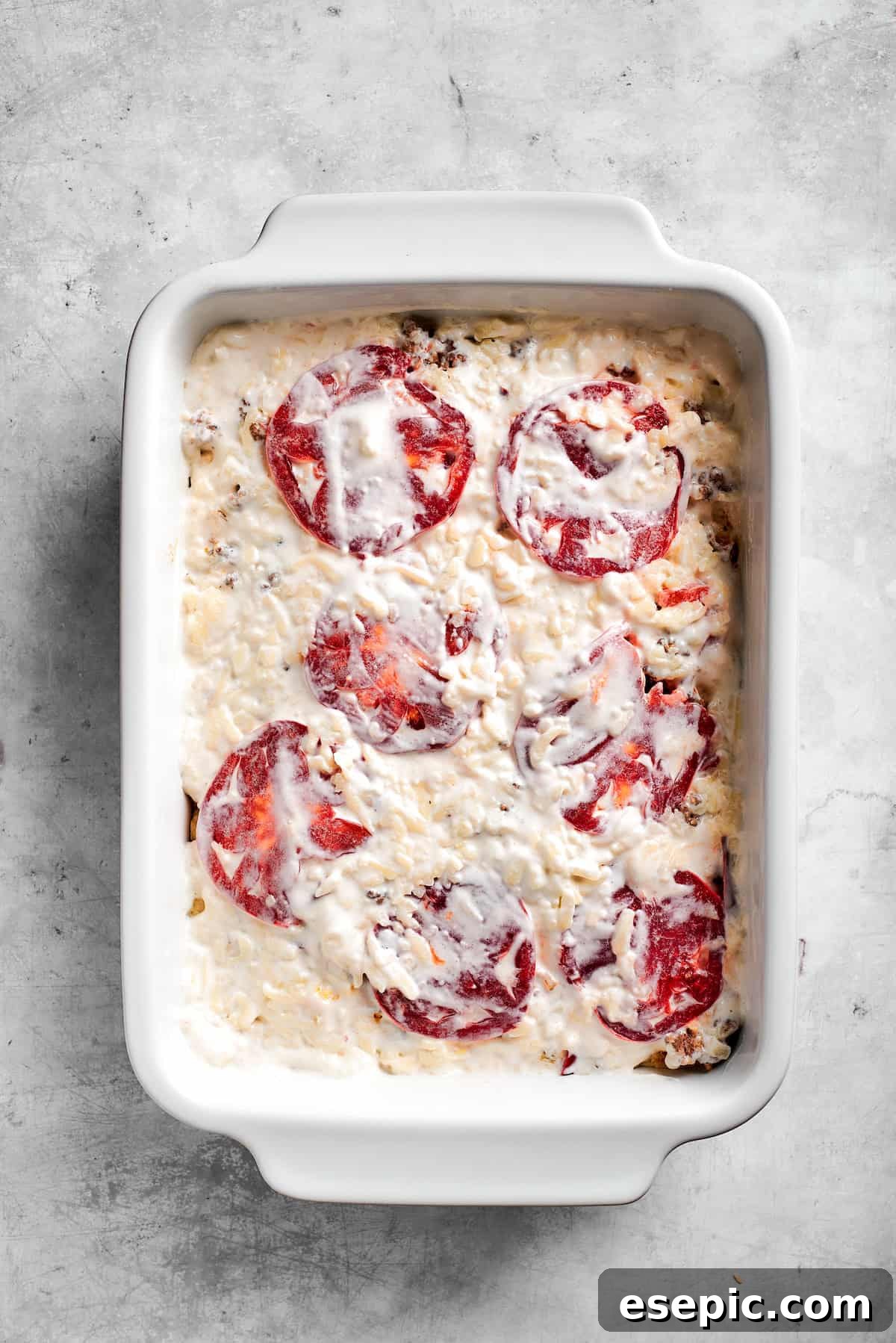The creamy sour cream and mayonnaise mixture being spread evenly over the tomato and chili layer in the casserole dish.