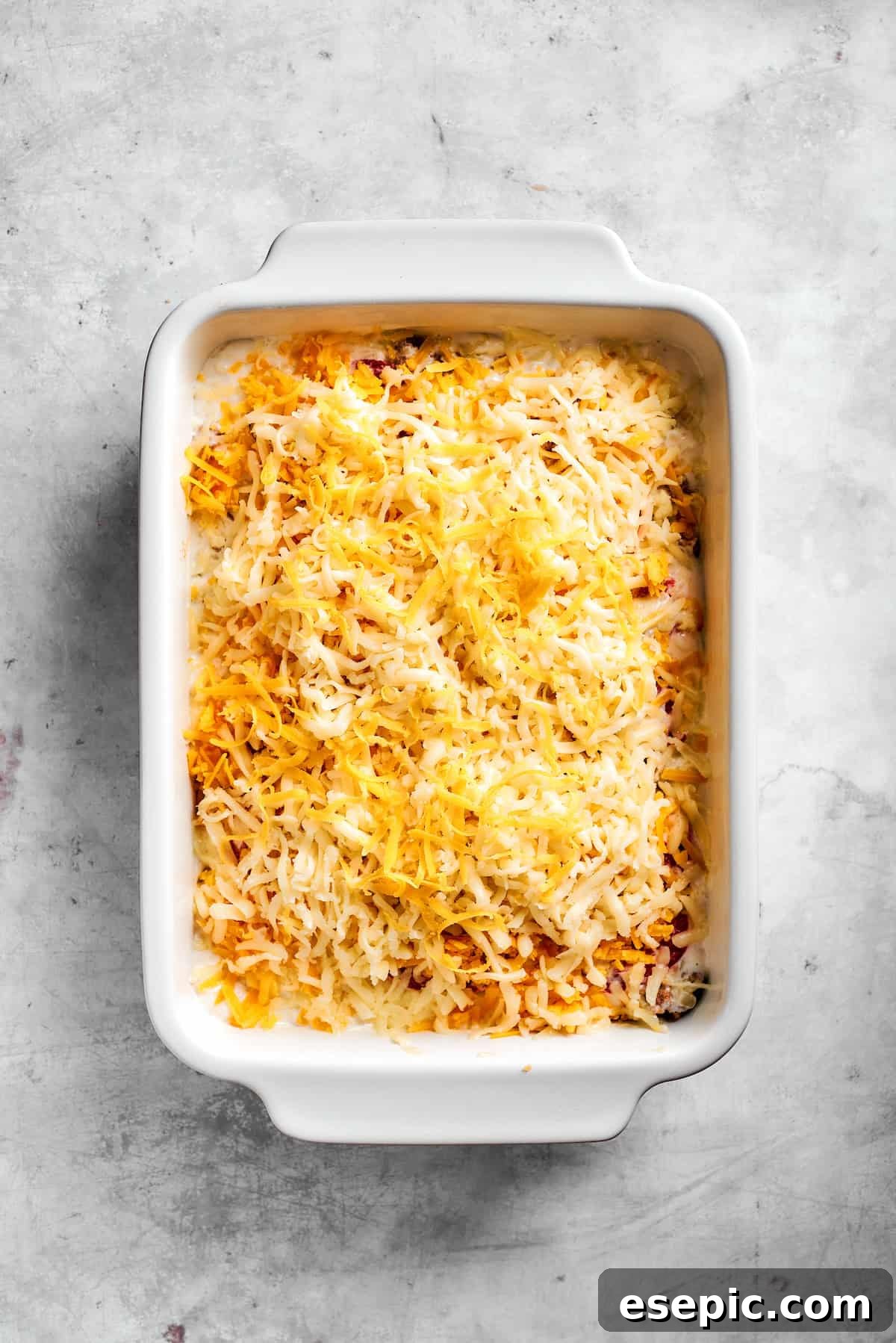 A generous layer of shredded cheddar and mozzarella cheese sprinkled over the assembled John Wayne Casserole, ready for baking.