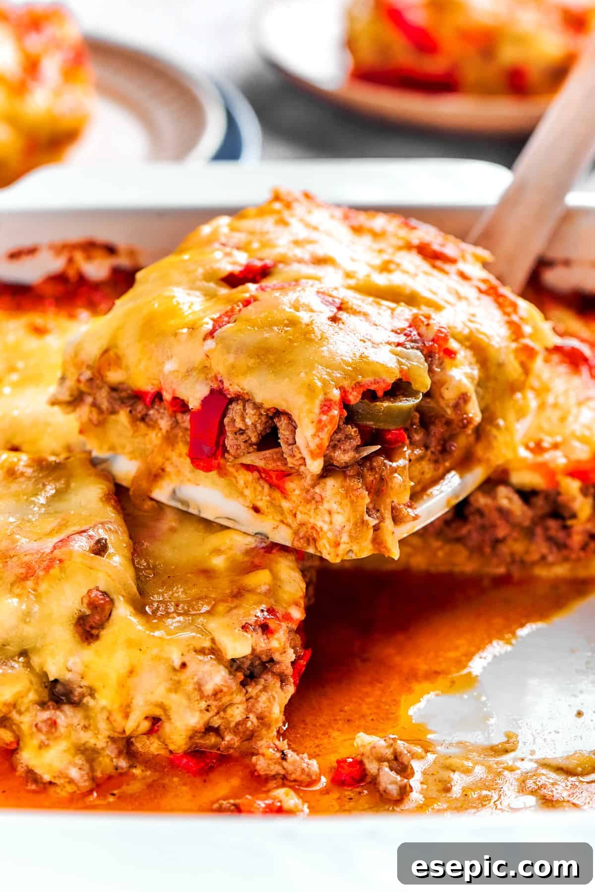 A large serving spoon scooping out a generous slice of the freshly baked John Wayne Casserole from the dish, revealing its distinct, flavorful layers.