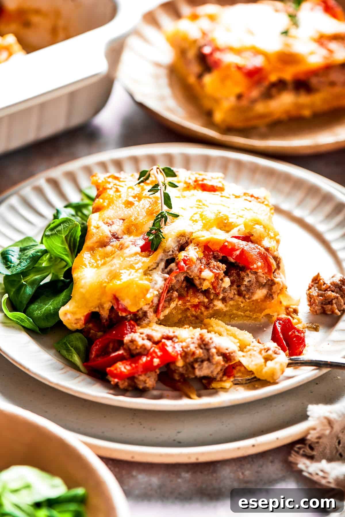 A generous slice of John Wayne Casserole, with visible layers of biscuit, beef, tomatoes, and cheese, served on a white dinner plate alongside a green salad.