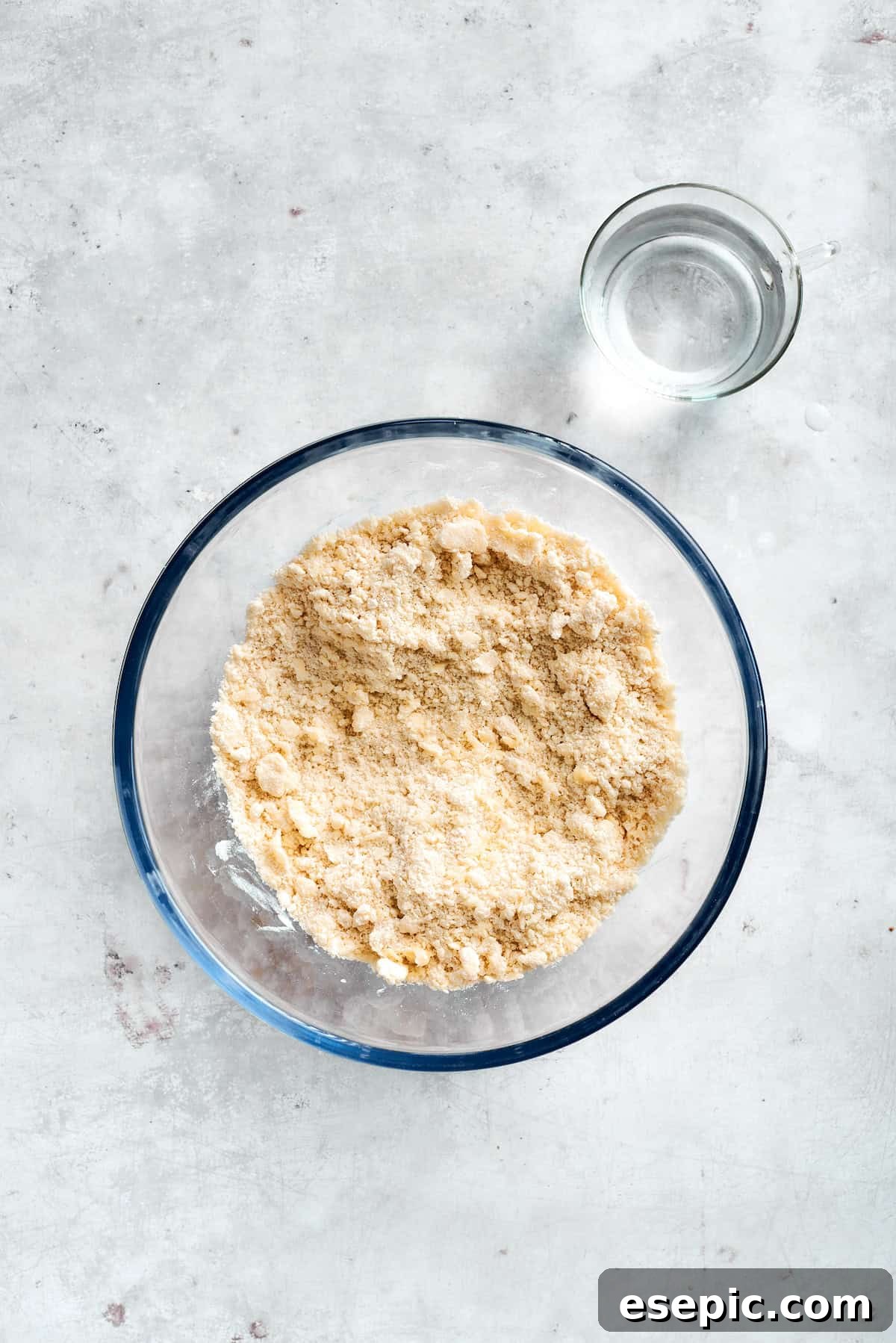 Bisquick mix and water being combined in a clear glass bowl, forming the dough for the casserole's biscuit base.