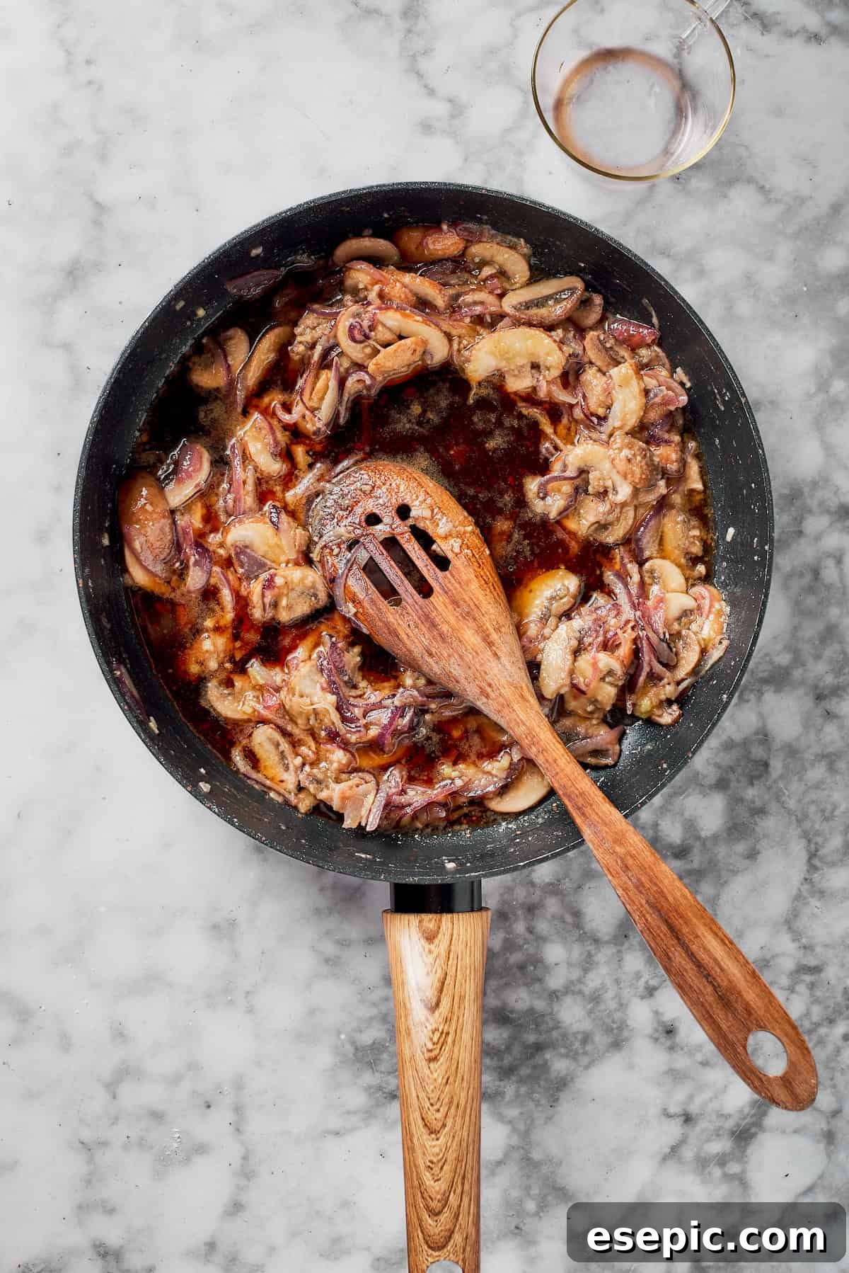 Marsala wine being poured into a skillet with sautéed mushrooms and onions, forming the sauce base.