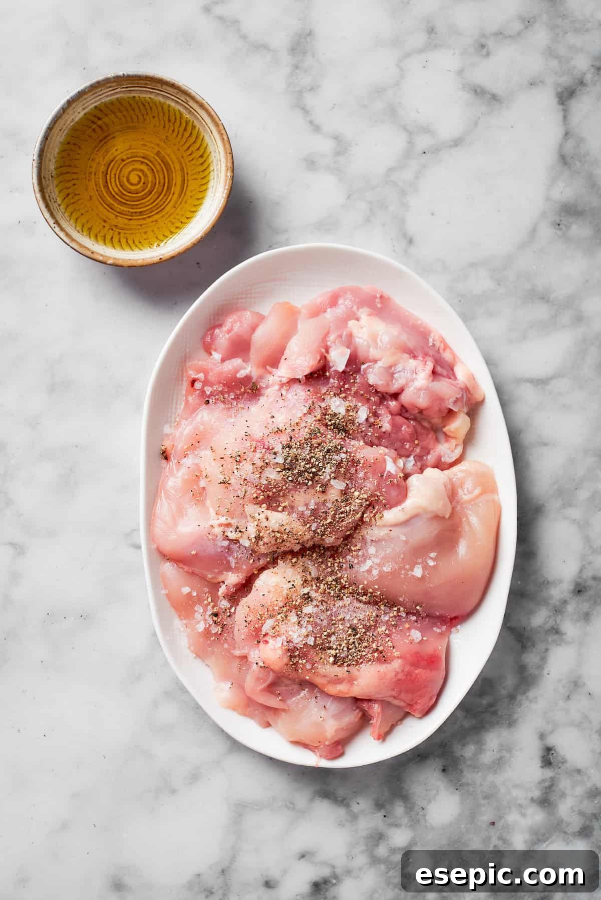Boneless, skinless chicken thighs seasoned with salt and pepper on a plate, ready for searing.