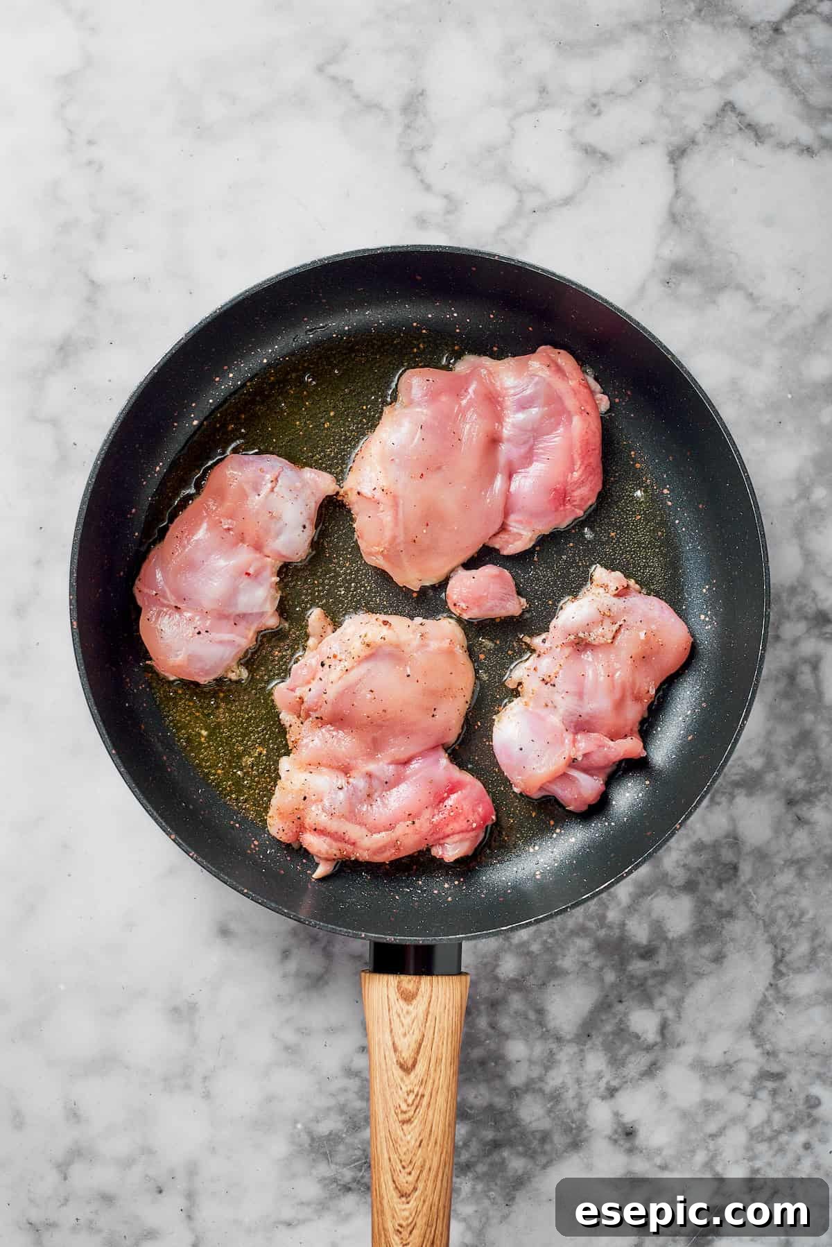 Chicken thighs searing in a hot skillet with olive oil, developing a golden crust.