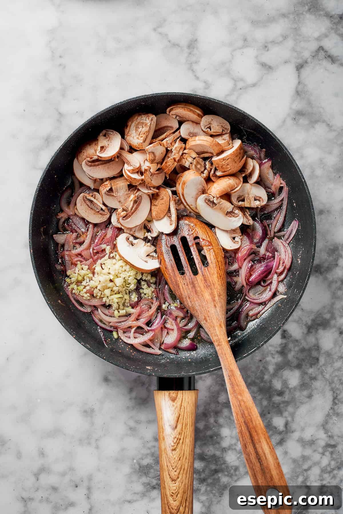 Cremini mushrooms and minced garlic being sautéed with caramelized onions in a pan.