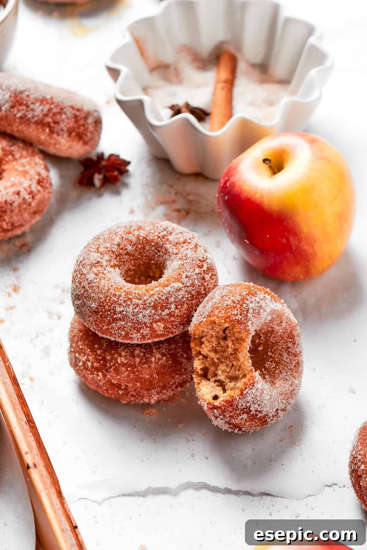 Baked not fried apple cider donuts are perfectly tender, dusted with spiced sugar, and fragrant with sweet apple cider. A little stack of baked apple cider donuts next to a fresh apple, evoking a classic autumn scene.