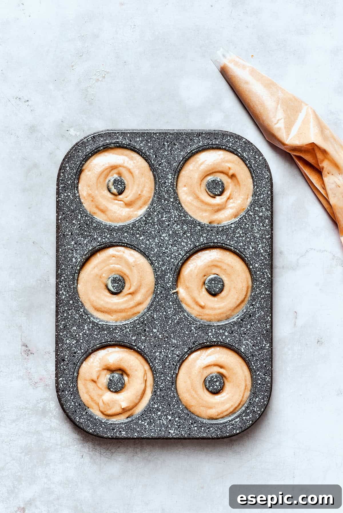 Baked not fried apple cider donuts are perfectly tender, dusted with spiced sugar, and fragrant with sweet apple cider. A donut pan with batter being piped into the wells for baking, showing precise filling.