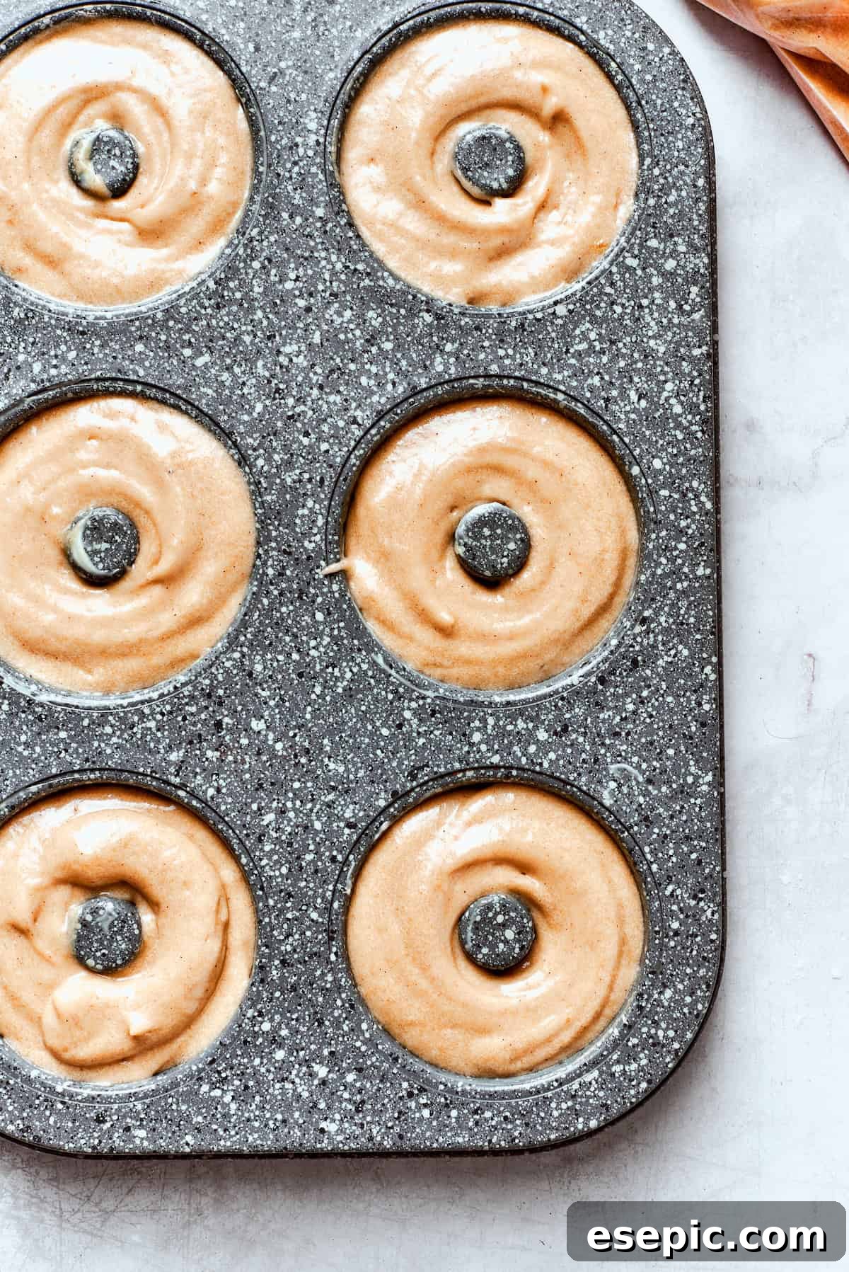 Baked not fried apple cider donuts are perfectly tender, dusted with spiced sugar, and fragrant with sweet apple cider. Apple cider donut batter neatly piped into a donut pan, ready for the oven.