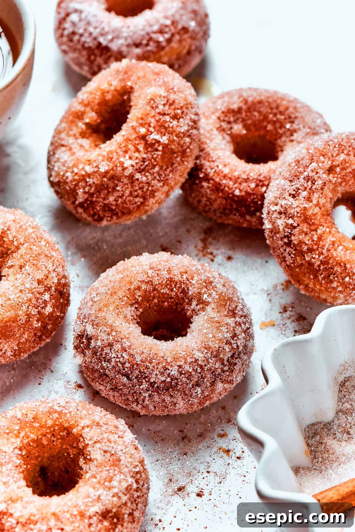 Baked not fried apple cider donuts are perfectly tender, dusted with spiced sugar, and fragrant with sweet apple cider. Cinnamon sugar sparkles on a fresh batch of baked apple cider donuts, glistening and ready to be enjoyed.