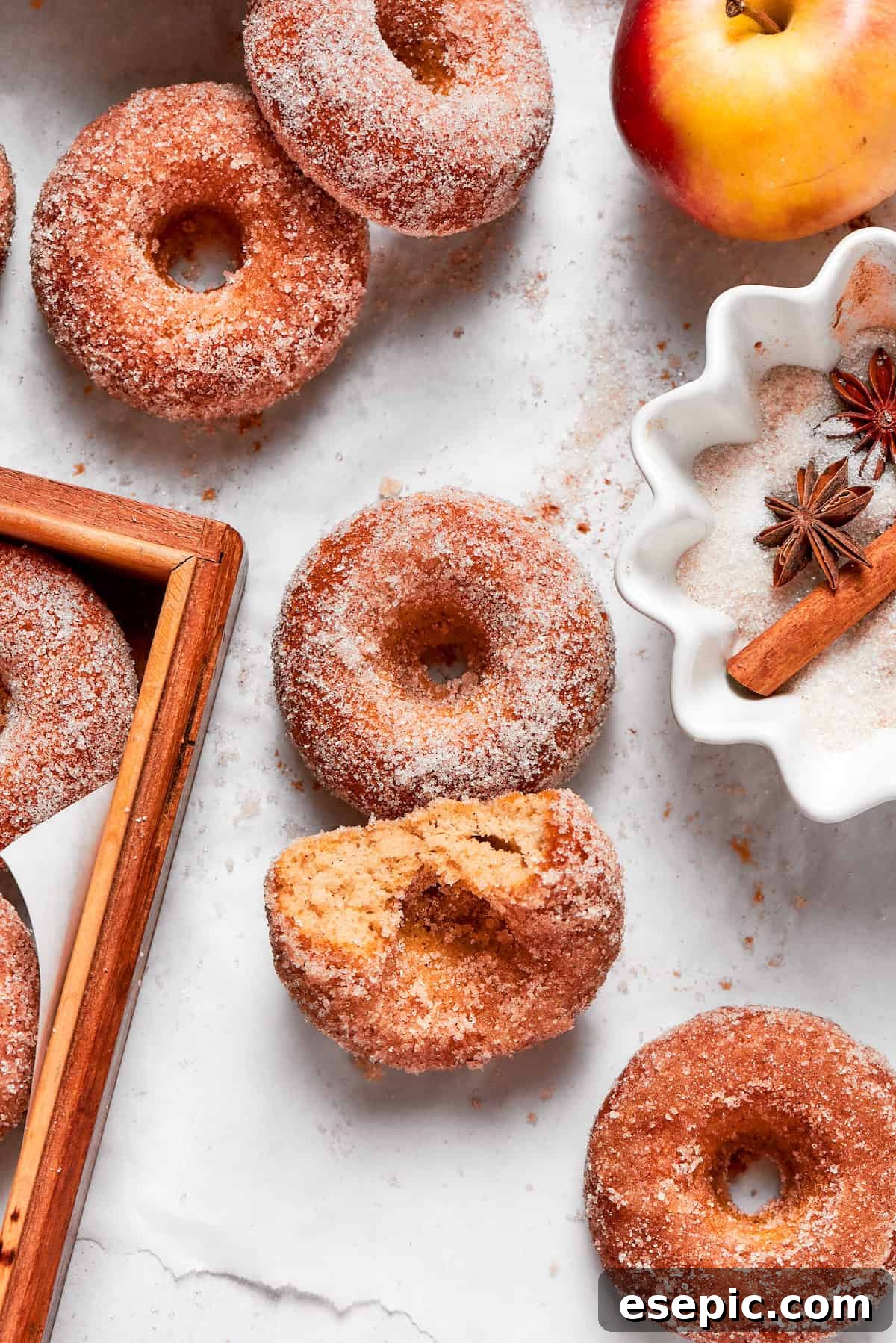 Baked not fried apple cider donuts are perfectly tender, dusted with spiced sugar, and fragrant with sweet apple cider. A freshly baked apple cider donut, with a bite taken out, revealing its soft, cake-like interior and glistening spiced sugar coating.