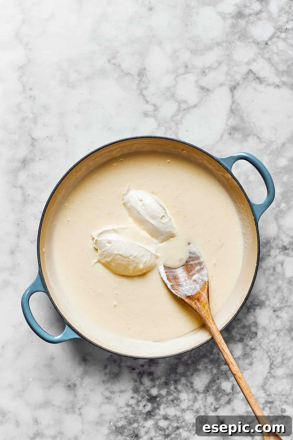 Creamy Garlic Parmesan Chicken Pasta 10 Cubed cream cheese being carefully added to the simmering creamy sauce in a pan, enhancing its richness.