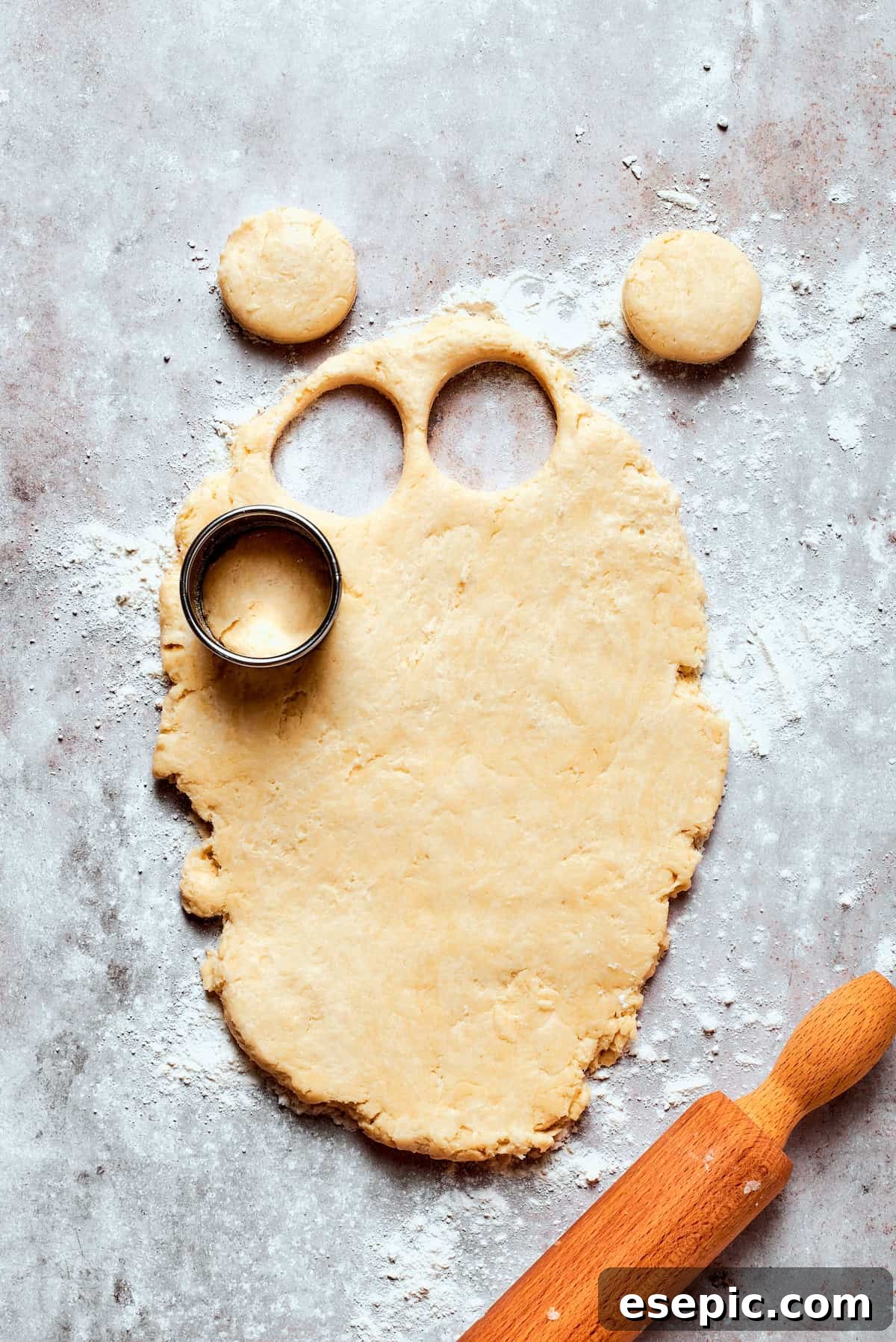 Cozy Chicken Pot Pie Casserole Recipe Round biscuit shapes being cut from rolled-out dough on a floured surface using a biscuit cutter.