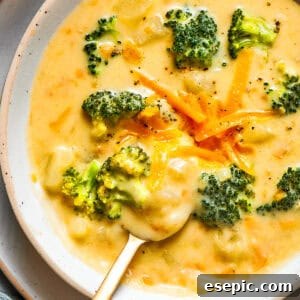 A steaming bowl of homemade broccoli cheese soup, garnished with shredded cheddar and fresh broccoli florets.